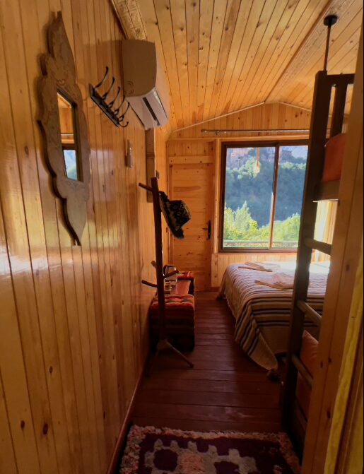 アトラス山脈イムリルのリヤドの客室。木目の部屋にベッドがあり、大きな窓の外に山の景色が見える